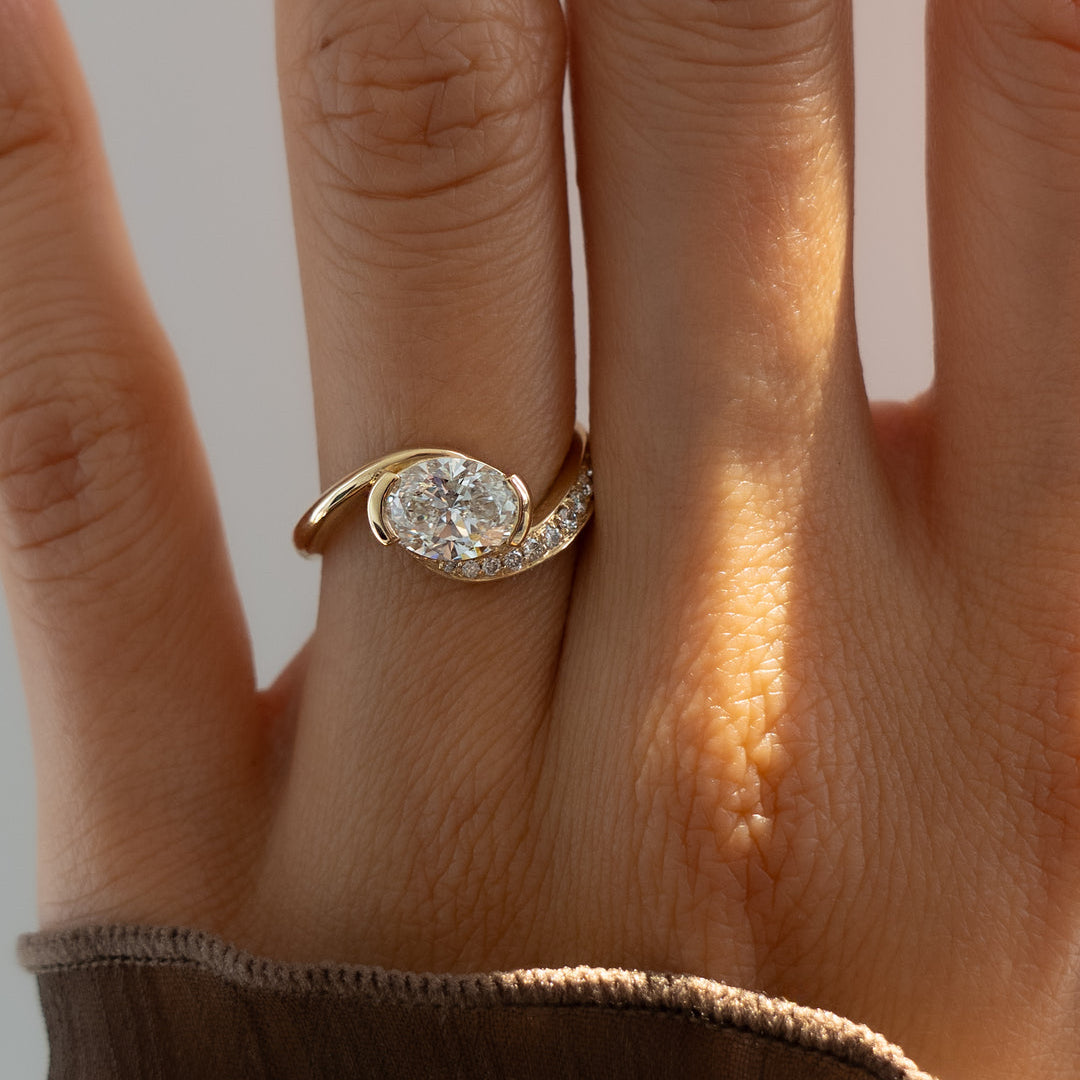 Gold ring with a diamond on a person's finger against a neutral background